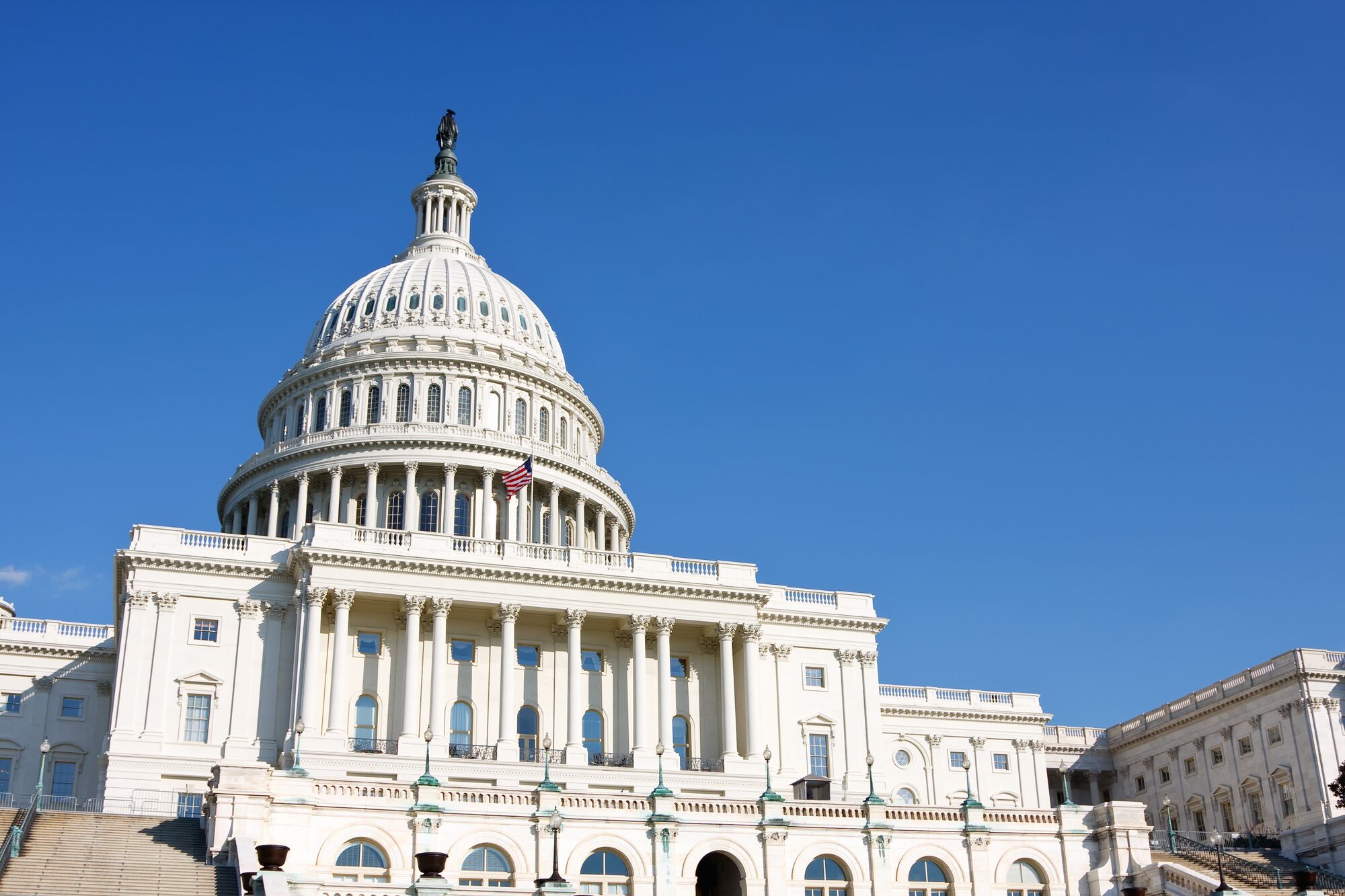 U.S. Capitol building with a prominent dome and statue atop, showcasing its neoclassical architecture against a clear blue sky.