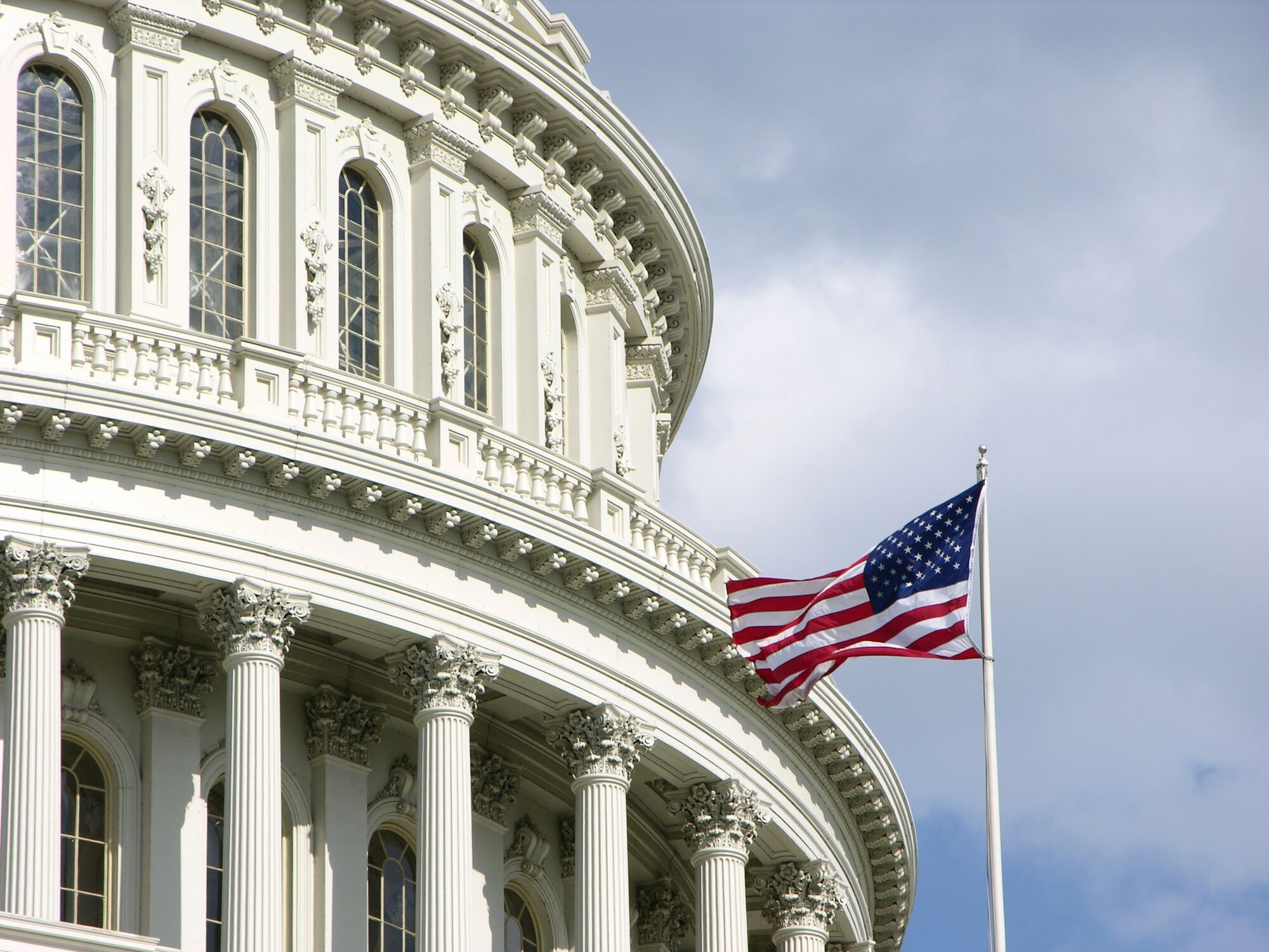 U.S. Capitol dome with American flag waving, showcasing architectural details and symbolizing national governance.